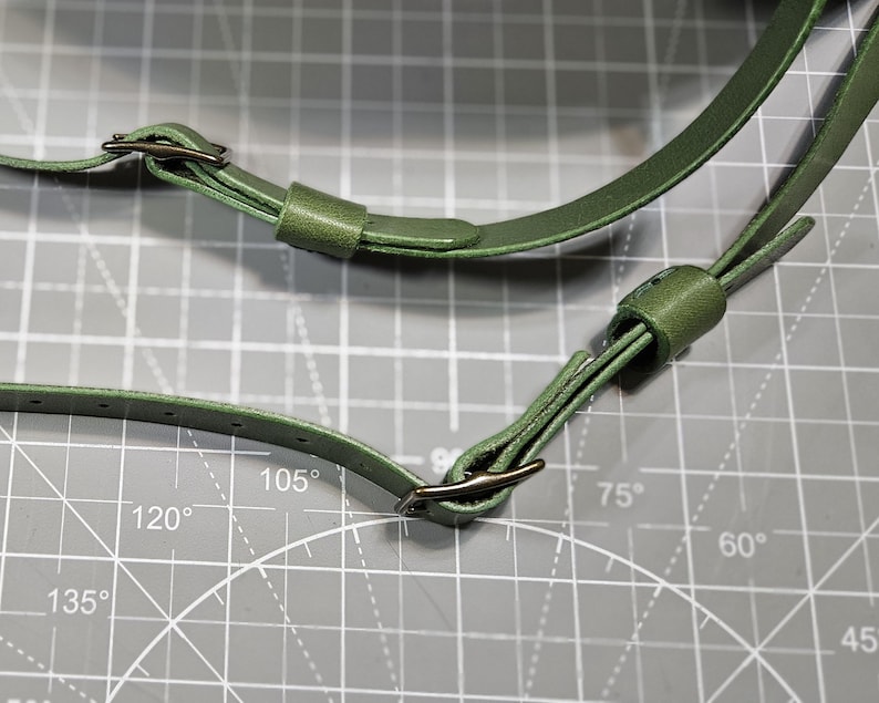 Puede incluir: Dos correas ajustables para bolso en color verde oliva con hebillas met&aacute;licas oscuras y trabillas deslizantes. Las correas presentan m&uacute;ltiples orificios preperforados para ajustar la longitud, con una textura lisa y bordes acabados.