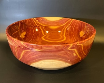 Puede incluir: Un tazón de madera grande de color marrón rojizo con un patrón de veta de madera natural. El tazón está hecho de una sola pieza de madera y tiene un acabado liso y pulido.