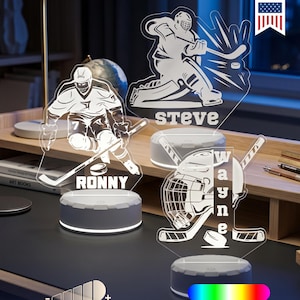 May include: Acrylic hockey-themed night lights with player illustrations and names: Ronny, Steve, and Wayne. Each light sits on a round base with 16 color options and dimmable settings. The lights are made in the USA.