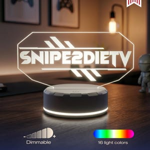 May include: A custom LED acrylic sign featuring the text SNIPE2DIETV in a stylized font, mounted on a circular white base. The sign is dimmable and capable of displaying 16 different light colors, with a Made in USA badge visible in the corner.