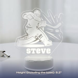 May include: A hockey-themed LED night light with the name "Steve" illuminated in white. The light features a hockey player graphic and a hockey puck. The base is white, and the height is 8.2 inches.