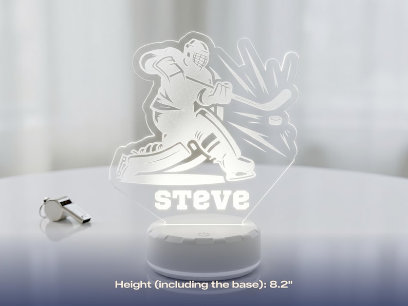 May include: A hockey-themed LED night light with the name "Steve" illuminated in white. The light features a hockey player graphic and a hockey puck. The base is white, and the height is 8.2 inches.