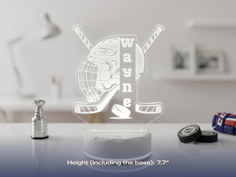 May include: A white hockey-themed LED lamp with the name "Wayne" vertically displayed. The lamp features a hockey helmet, sticks, and a puck design. The base is white, and the height, including the base, is 7.7 inches.
