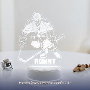 May include: A hockey-themed LED lamp featuring a player graphic, the name "RONNY", and a hockey puck. The lamp is 7.8 inches tall, including the base. A miniature hockey helmet and a whistle are also visible.