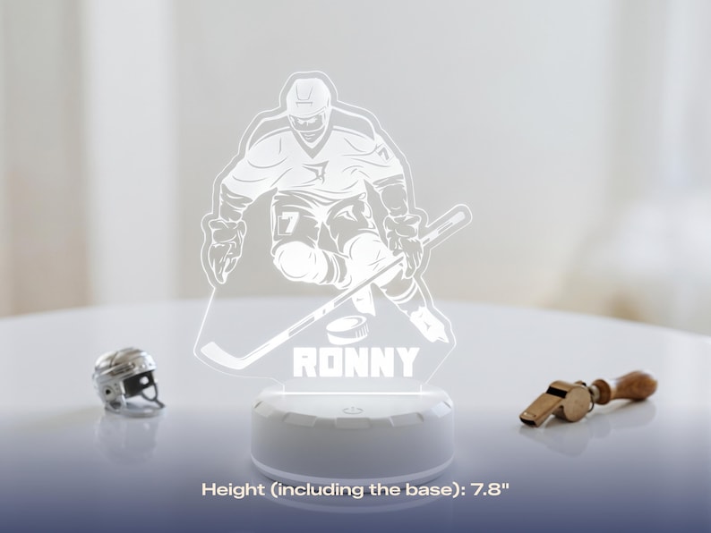 May include: A hockey-themed LED lamp featuring a player graphic, the name "RONNY", and a hockey puck. The lamp is 7.8 inches tall, including the base. A miniature hockey helmet and a whistle are also visible.