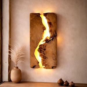 Può includere: Applique da parete rettangolare in legno con una fessura luminosa gialla al centro. Il legno è marrone chiaro con dettagli strutturati più scuri. L'applique è montata su una parete beige chiaro.