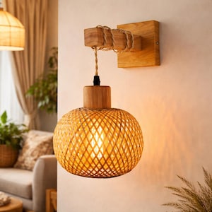 以下が含まれることがあります： 編み込まれたラタンシェードの壁掛け照明器具。器具は木製のベースと円筒形の木製上部を備えています。シェードは暖かく自然な色で、ライトが点灯しています。屋内での使用向けに設計されています。
