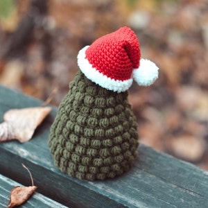May include: A small green crocheted Christmas tree with a red and white Santa hat.