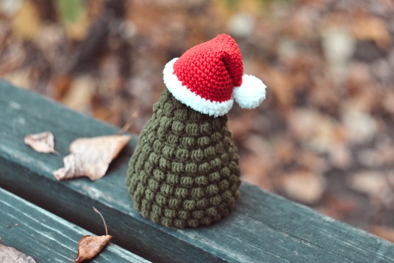 May include: A small green crocheted Christmas tree with a red and white Santa hat.