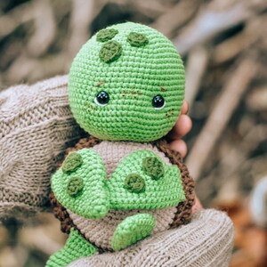 Pu&ograve; includere: Una tartaruga all'uncinetto fatta a mano nei toni del verde, marrone e beige. La tartaruga ha una testa verde arrotondata con occhi scuri e macchie verdi decorative. Il guscio &egrave; marrone e beige, con appendici verdi a forma di pinna. Un giocattolo morbido.