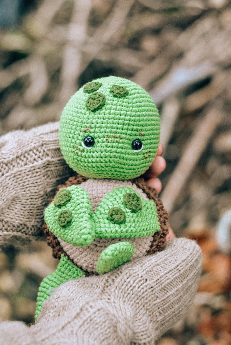 Pu&ograve; includere: Una tartaruga all'uncinetto fatta a mano nei toni del verde, marrone e beige. La tartaruga ha una testa verde arrotondata con occhi scuri e macchie verdi decorative. Il guscio &egrave; marrone e beige, con appendici verdi a forma di pinna. Un giocattolo morbido.