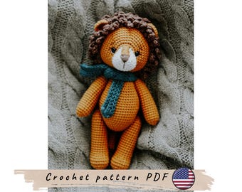 May include: A handmade crochet lion doll with a brown mane, orange body, and a blue scarf. The lion is sitting on a gray knitted blanket. The image includes the text "Crochet pattern PDF".