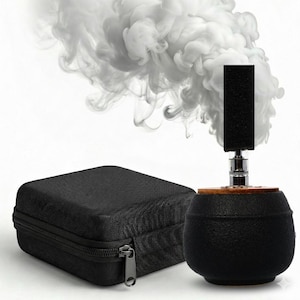 Puede incluir: Un vaporizador esférico negro con un acento de madera y una parte superior rectangular negra. Un estuche negro con cremallera está a la izquierda. El vapor blanco se eleva del vaporizador sobre un fondo blanco.