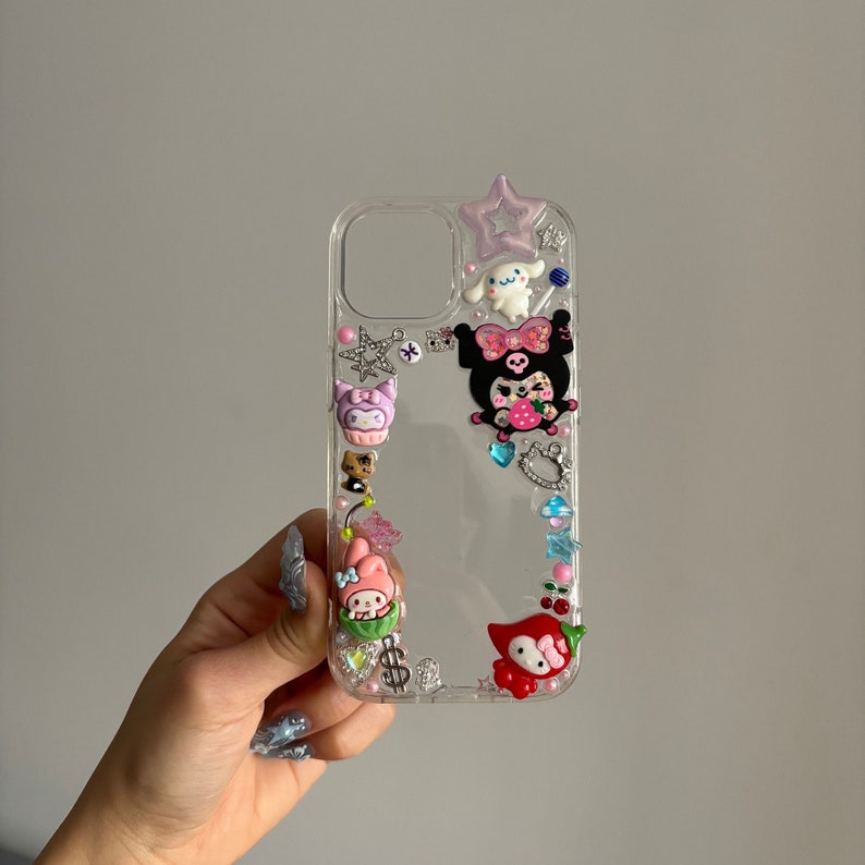 May include: Clear phone case with a variety of colorful cartoon characters and embellishments, including a pink and black character with a strawberry, a pink character with bunny ears, and a red chili pepper.
