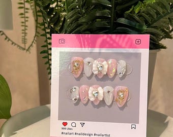 May include: Pink and white press-on nails with a 3D bow and bear design. The nails are decorated with rhinestones and glitter. #nailart #naildesigns #nailartist