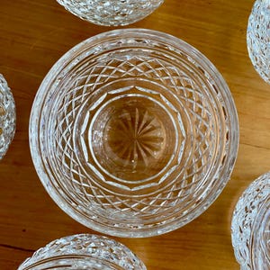 Puede incluir: Vista cenital de varios cuencos de cristal tallado transparente con intrincados dise&ntilde;os de diamantes y estrellas. Los cuencos est&aacute;n dispuestos sobre una superficie de madera de tonos c&aacute;lidos, mostrando sus cualidades reflectantes y su elegante dise&ntilde;o.