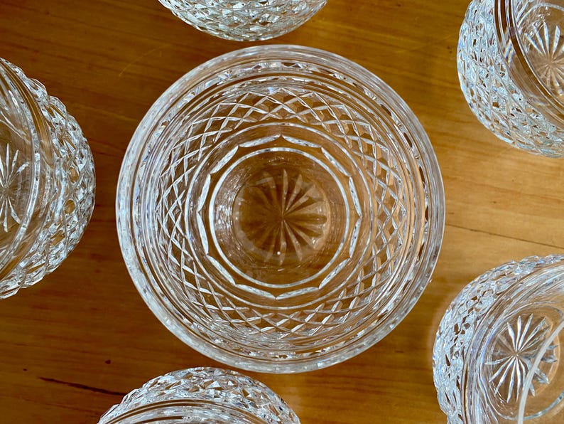 Puede incluir: Vista cenital de varios cuencos de cristal tallado transparente con intrincados dise&ntilde;os de diamantes y estrellas. Los cuencos est&aacute;n dispuestos sobre una superficie de madera de tonos c&aacute;lidos, mostrando sus cualidades reflectantes y su elegante dise&ntilde;o.