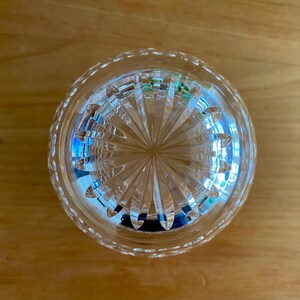 Puede incluir: Un vaso transparente y redondo con un patr&oacute;n grabado detallado. El vaso tiene un dise&ntilde;o de estrella en la parte inferior y un borde con cuentas. El vaso est&aacute; sobre una superficie de madera. Probablemente sea un vaso para beber o un objeto decorativo.