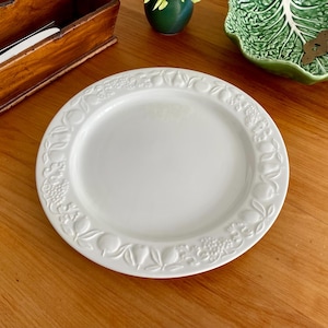 May include: A white ceramic dinner plate with a raised design of fruit and leaves around the rim.