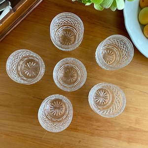 Puede incluir: Seis cuencos peque&ntilde;os de vidrio tallado transparente, con un dise&ntilde;o de estrella en la base y un patr&oacute;n de diamantes en los lados, est&aacute;n dispuestos sobre una superficie de madera. Una caja de madera con cubiertos est&aacute; en la esquina superior izquierda.