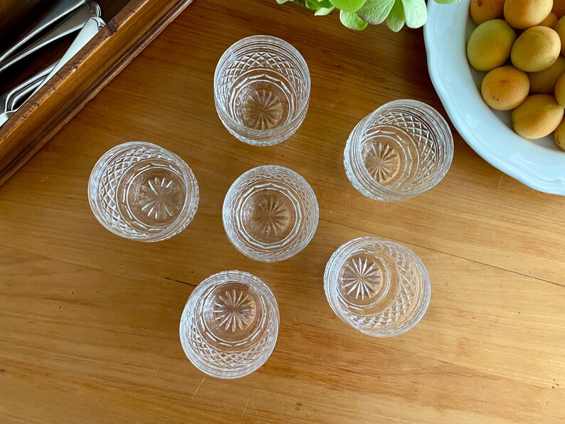 Puede incluir: Seis cuencos peque&ntilde;os de vidrio tallado transparente, con un dise&ntilde;o de estrella en la base y un patr&oacute;n de diamantes en los lados, est&aacute;n dispuestos sobre una superficie de madera. Una caja de madera con cubiertos est&aacute; en la esquina superior izquierda.