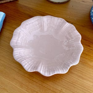 May include: A pale pink ceramic bowl with a scalloped edge and a textured surface. The bowl is empty and appears to be made for serving small items.