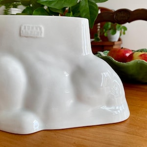 May include: White ceramic mould shaped like a reclining rabbit. The mould has a raised inscription that reads "Made in England".