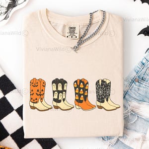 Puede incluir: Camiseta color marfil con cuatro botas de vaquero con dise&ntilde;os de Halloween. Las botas son naranjas, negras y blancas, con calabazas, fantasmas, caramelos y telara&ntilde;as. La camiseta tiene una etiqueta Comfort Colors y se combina con pantalones cortos vaqueros.
