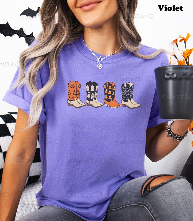 Puede incluir: Una camiseta violeta con un gr&aacute;fico de cuatro botas de vaquero con tem&aacute;tica de Halloween. Las botas est&aacute;n decoradas con calabazas, fantasmas, caramelos y telara&ntilde;as. El texto "Violet" es visible en la esquina superior derecha.