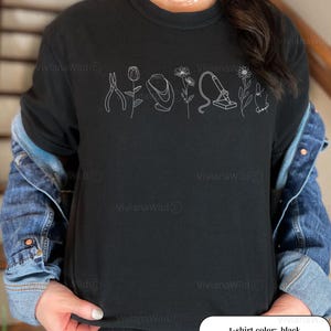 May include: Black crew neck t-shirt with a white line drawing of tools and flowers. The shirt has the text "t-shirt color: black" at the bottom. The shirt is worn with a denim jacket.