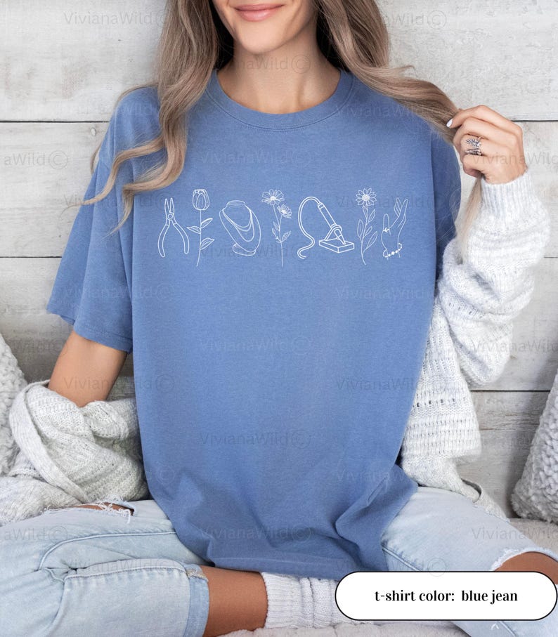May include: Blue jean colored t-shirt with a white line drawing of tools and flowers. The text "t-shirt color: blue jean" is at the bottom of the image. The shirt is a comfortable, casual style.
