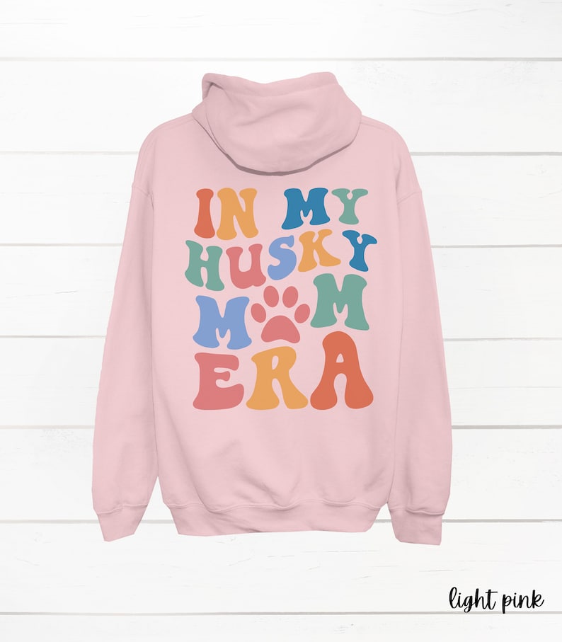 May include: Light pink hooded sweatshirt with the text "In My Husky Mom Era" in rainbow colors with a paw print in the middle of the word "Mom".