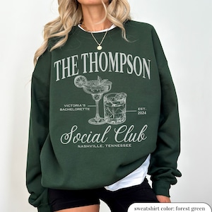 May include: Forest green sweatshirt with white text that reads "THE THOMPSON VICTORIA'S BACHELORETTE EST. 2024 Social Club NASHVILLE. TENNESSEE". The design features two cocktail glasses.