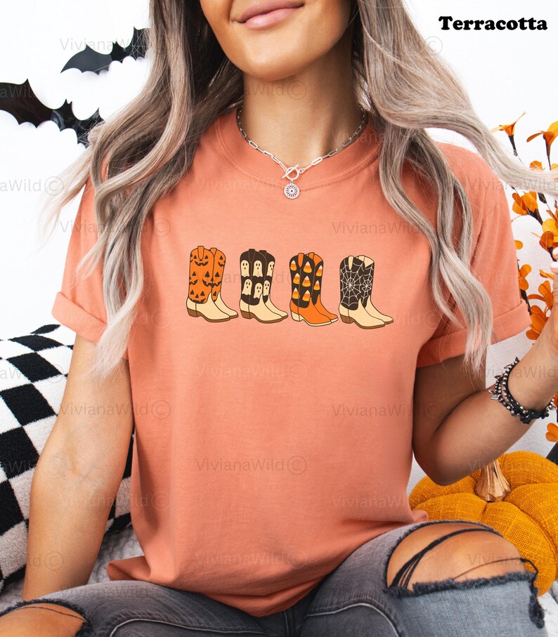 Puede incluir: Camiseta color terracota con una fila de botas de vaquero de dibujos animados con dise&ntilde;os de Halloween. Las botas incluyen calabazas, fantasmas, caramelos de ma&iacute;z y telara&ntilde;as. El texto "Terracota" est&aacute; en la esquina superior derecha.