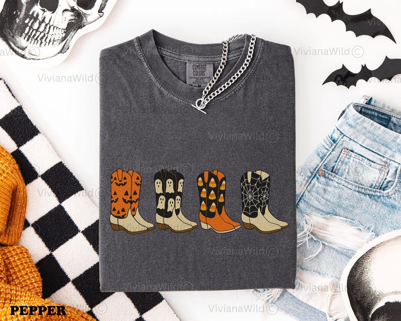 Puede incluir: Camiseta gris oscuro Comfort Colors con cuatro dise&ntilde;os de botas de vaquero con tem&aacute;tica de Halloween. Las botas son naranjas, negras y blancas, con calabazas, fantasmas, caramelos y telara&ntilde;as. Un collar de cadena plateada est&aacute; sobre la camisa.