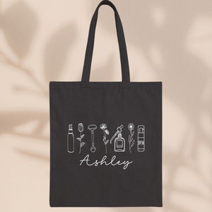 Peut inclure: Sac fourre-tout en toile noire avec un contour blanc de divers produits de soin de la peau et le nom "Ashley" imprim&eacute; sur le devant.