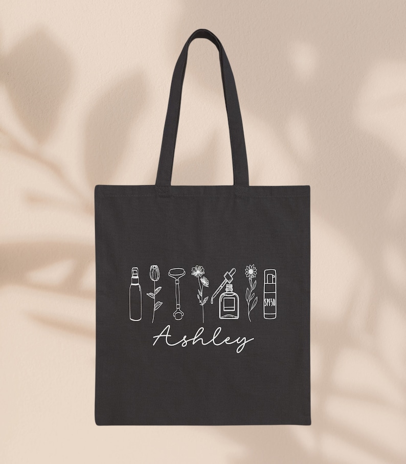 Peut inclure: Sac fourre-tout en toile noire avec un contour blanc de divers produits de soin de la peau et le nom "Ashley" imprim&eacute; sur le devant.