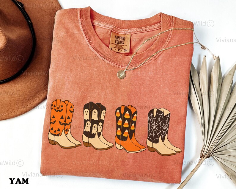 Puede incluir: Una camiseta de color coral con cuatro dise&ntilde;os de botas de vaquero con tem&aacute;tica de Halloween. Las botas est&aacute;n decoradas con calabazas, fantasmas, caramelos de ma&iacute;z y telara&ntilde;as. La camiseta tiene cuello redondo y una etiqueta peque&ntilde;a que dice "Comfort Colors".