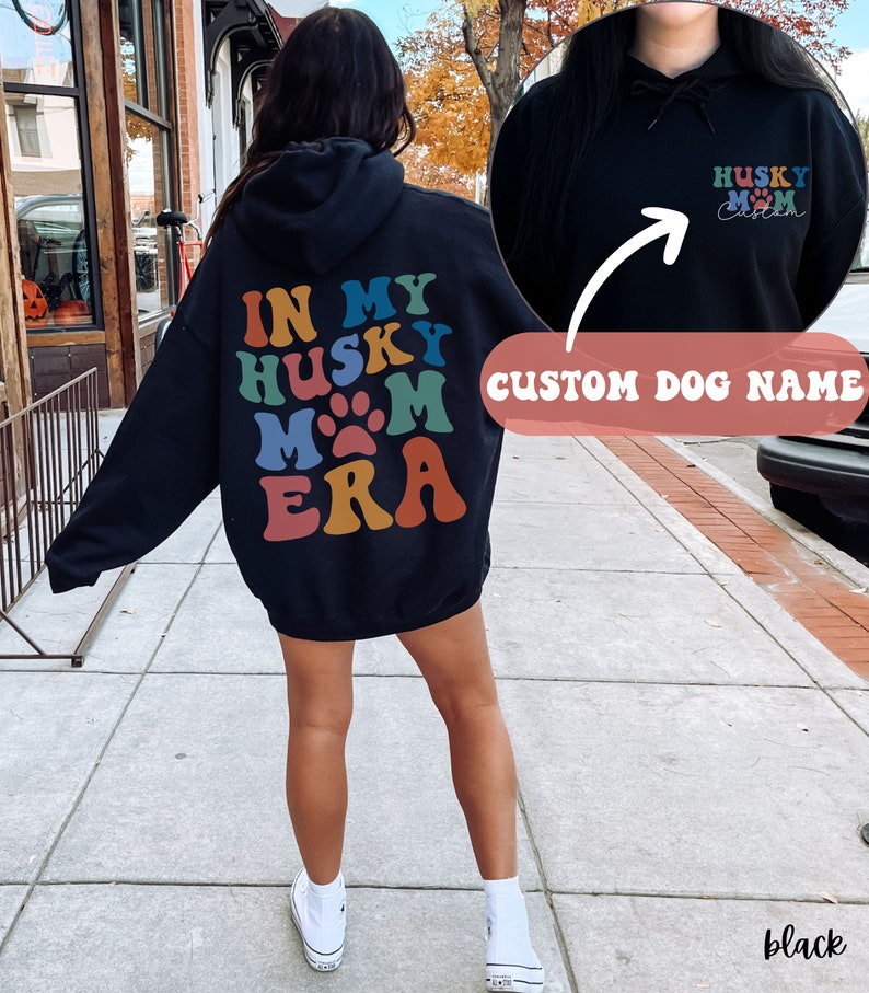 May include: Black hooded sweatshirt with the text "In My Husky Mom Era" in rainbow colors on the back. The front of the sweatshirt has the text "Husky Mom" with a paw print and space for a custom dog name.