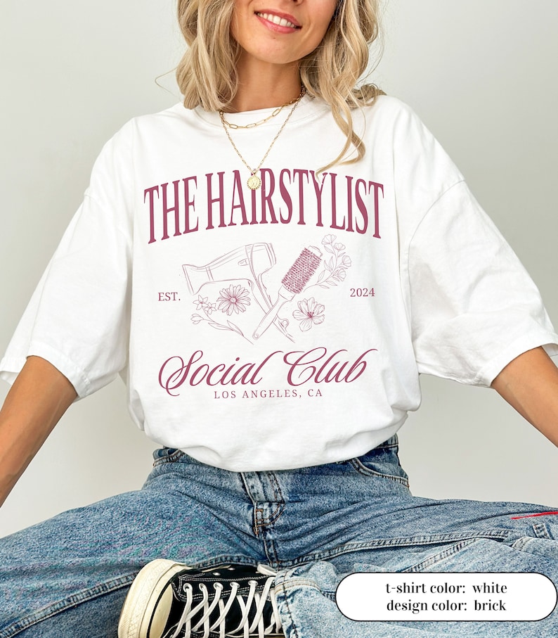 May include: White t-shirt with a brick-colored design. The design includes the text "THE HAIRSTYLIST Social Club LOS ANGELES, CA" with a hairdryer, brush, and floral accents. The year "2024" is also included in the design.