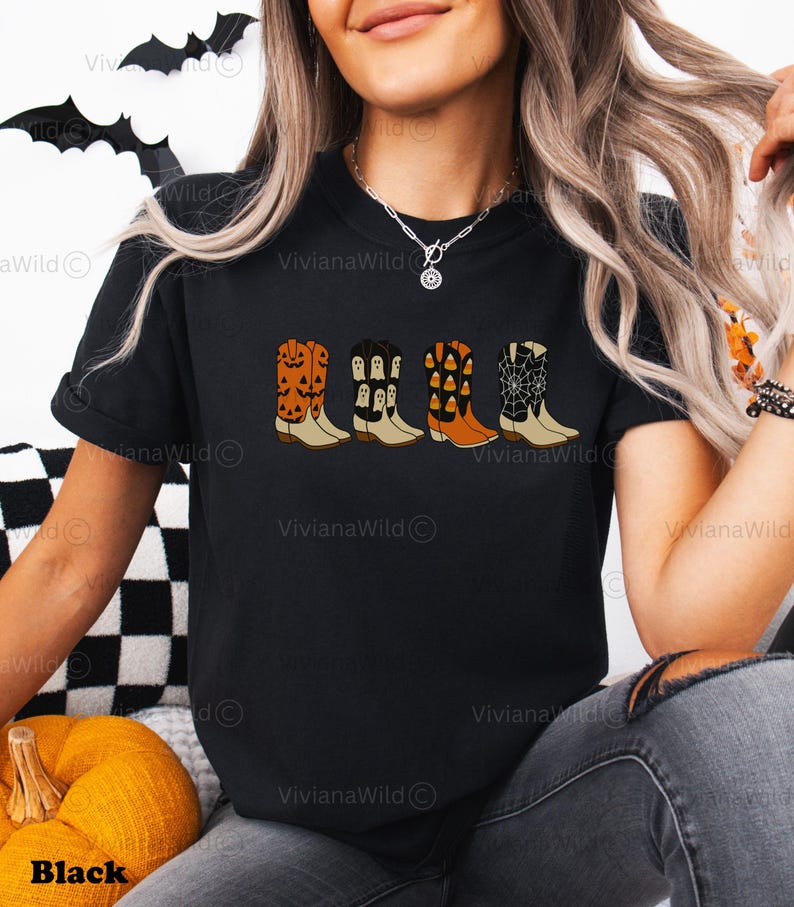 Puede incluir: Camiseta negra con un dise&ntilde;o de cuatro botas de vaquero decoradas con motivos de Halloween. Las botas presentan calabazas, fantasmas, caramelos de ma&iacute;z y telara&ntilde;as. La camiseta tiene cuello redondo y la palabra "Black" est&aacute; en la parte inferior.