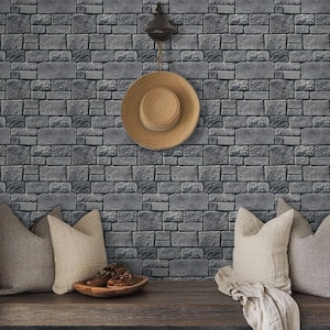 May include: A grey brick wall with a straw hat hanging on a hook. Two cushions are on a wooden bench in front of the wall.