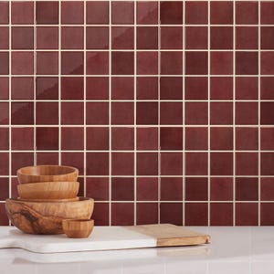 May include: Wooden bowls of different sizes are stacked on a white chopping board with a wooden handle. The background features a wall of square, burgundy tiles with white grout.
