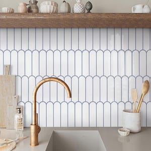May include: White ceramic subway tiles with a blue arched design, a gold faucet, and a white ceramic utensil holder with wooden utensils.