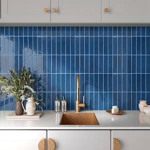 Puede incluir: Un área de fregadero de cocina con una cubeta rectangular de tono cobre, un grifo alto de latón y un salpicadero de azulejos rectangulares verticales de color azul oscuro brillante. Una jarra de cerámica blanca con plantas está a la izquierda.
