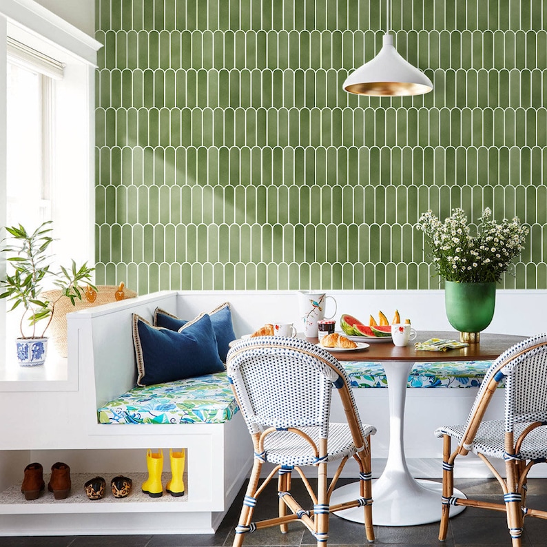 K&ouml;nnte beinhalten: Ein heller, einladender Fr&uuml;hst&uuml;cksbereich mit einem runden Holztisch und zwei Korbst&uuml;hlen. Der Raum verf&uuml;gt &uuml;ber eine eingebaute wei&szlig;e Bank mit blauen Kissen und einem floralen Kissen. Eine gr&uuml;n-wei&szlig;e Fliesenwand bildet einen stilvollen Hintergrund.
