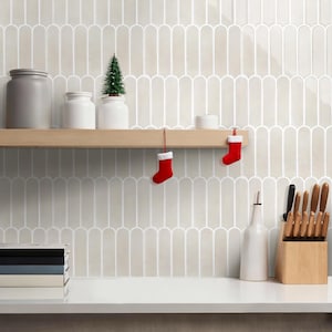 Può includere: Scena cucina dai toni neutri. Una mensola in legno espone un piccolo albero di Natale, barattoli e due calzini rossi di Natale. Una pila di libri e un ceppo portacoltelli sono sul bancone. La parete presenta un motivo di piastrelle decorative.