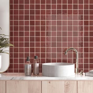 Könnte beinhalten: Ein Badezimmer-Waschtischbereich mit einem weißen zylindrischen Aufsatzwaschbecken und einer hohen, geschwungenen Chromarmatur. Die Wand hinter dem Waschbecken ist mit quadratischen, glänzenden, dunkelroten Fliesen mit hellen Fugen verkleidet.
