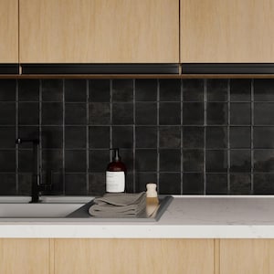 Könnte beinhalten: Eine moderne Küchenszene mit schwarzem Wasserhahn, Spüle und Fliesenspiegel. Ein brauner Seifenspender, ein graues gefaltetes Handtuch und eine kleine Bürste stehen auf einem Tablett aus Edelstahl. Helle Holzschränke befinden sich über dem Fliesenspiegel.