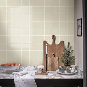 May include: A kitchen scene with a marble countertop and a light green tiled wall. A wooden cutting board, a small Christmas tree, and a lit candle are on the counter. A bowl of oranges and a decorative towel are also present.